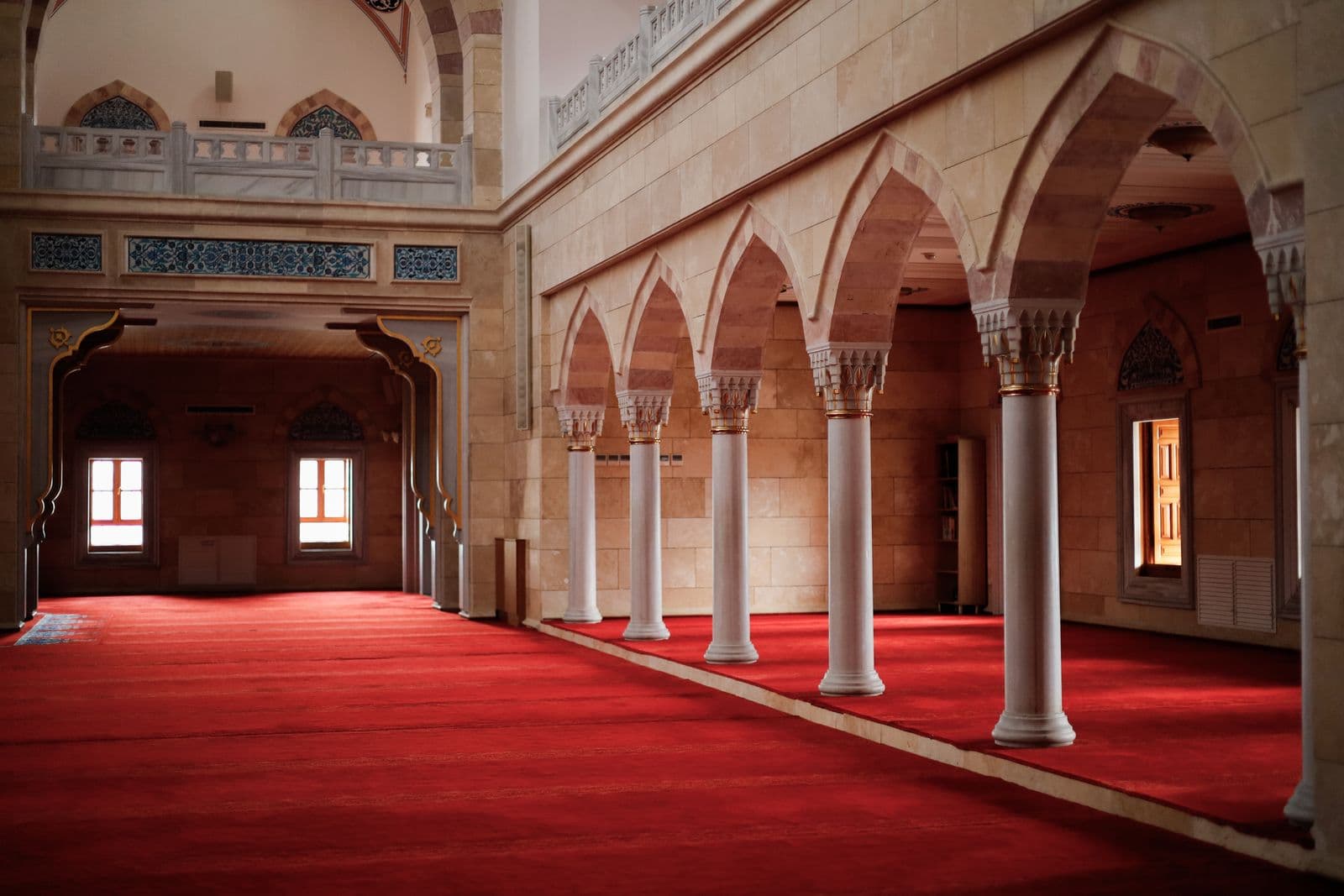 Sunlit arches and red prayer carpet in a mosque; illustrative stock photography